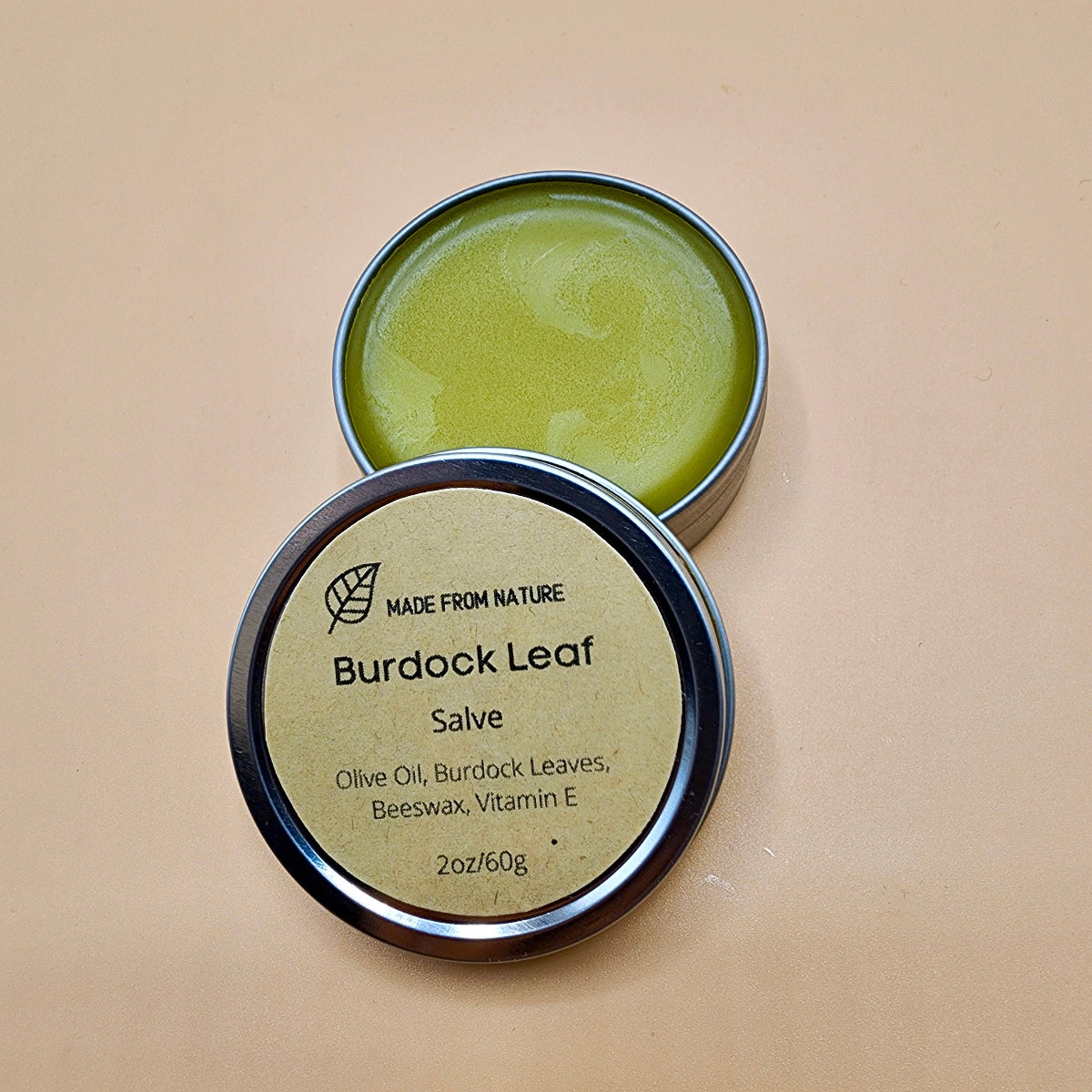 Burdock Leaf Salve in a metal tin on a beige background. Contains compounds that protect cells from damage and reduce inflammation.