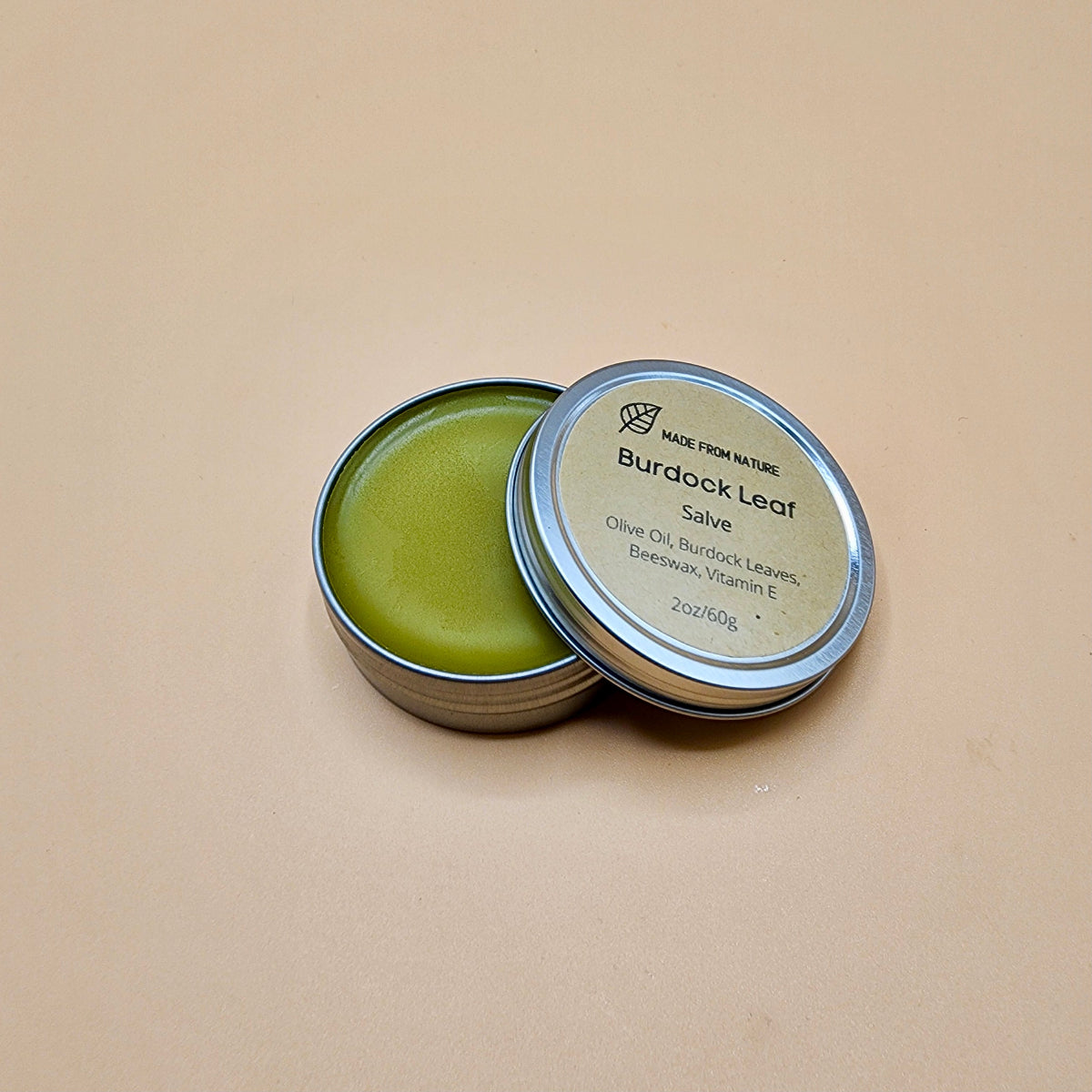 Burdock Leaf Salve in a metal tin on a beige background, Effective for treating eczema, psoriasis, acne, and reducing redness and inflammation.